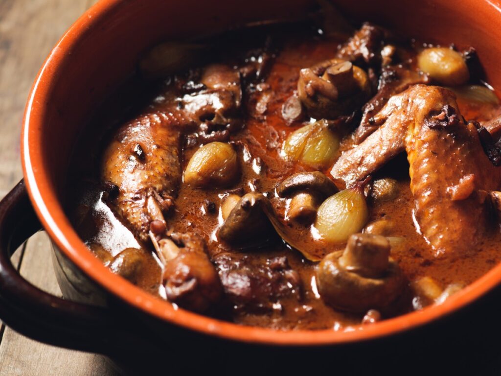 Coq au Vin in a Dutch oven with chicken, mushrooms, pearl onions, and red wine sauce
