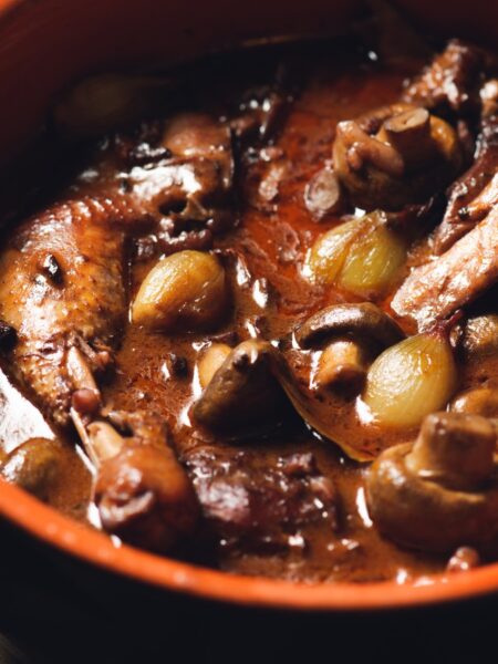 Coq au Vin in a Dutch oven with chicken, mushrooms, pearl onions, and red wine sauce
